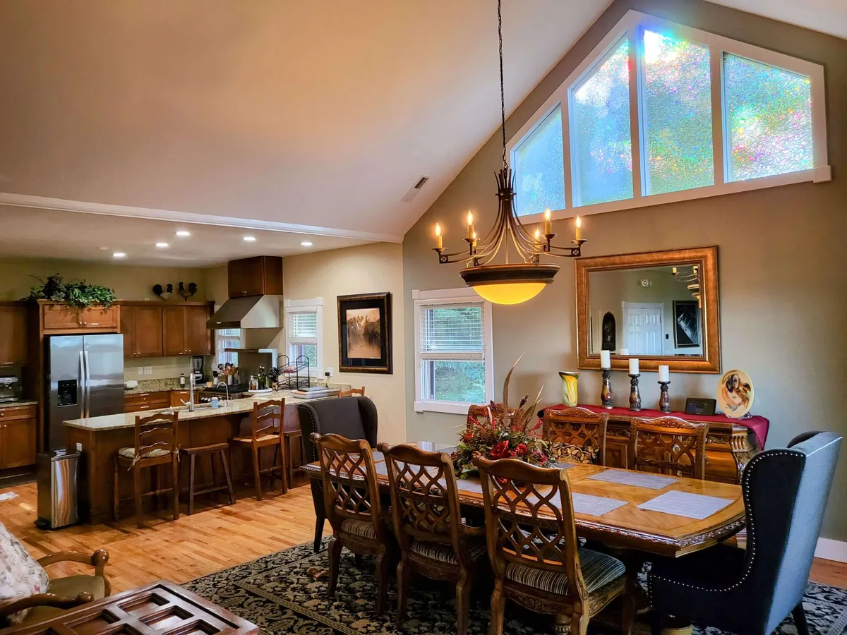 A beautifully arranged dining table set beside a kitchen island, illuminated by a stained glass window and chandelier. The setting is ideal for family meals or festive gatherings, with ample space and natural light enhancing the welcoming ambiance.