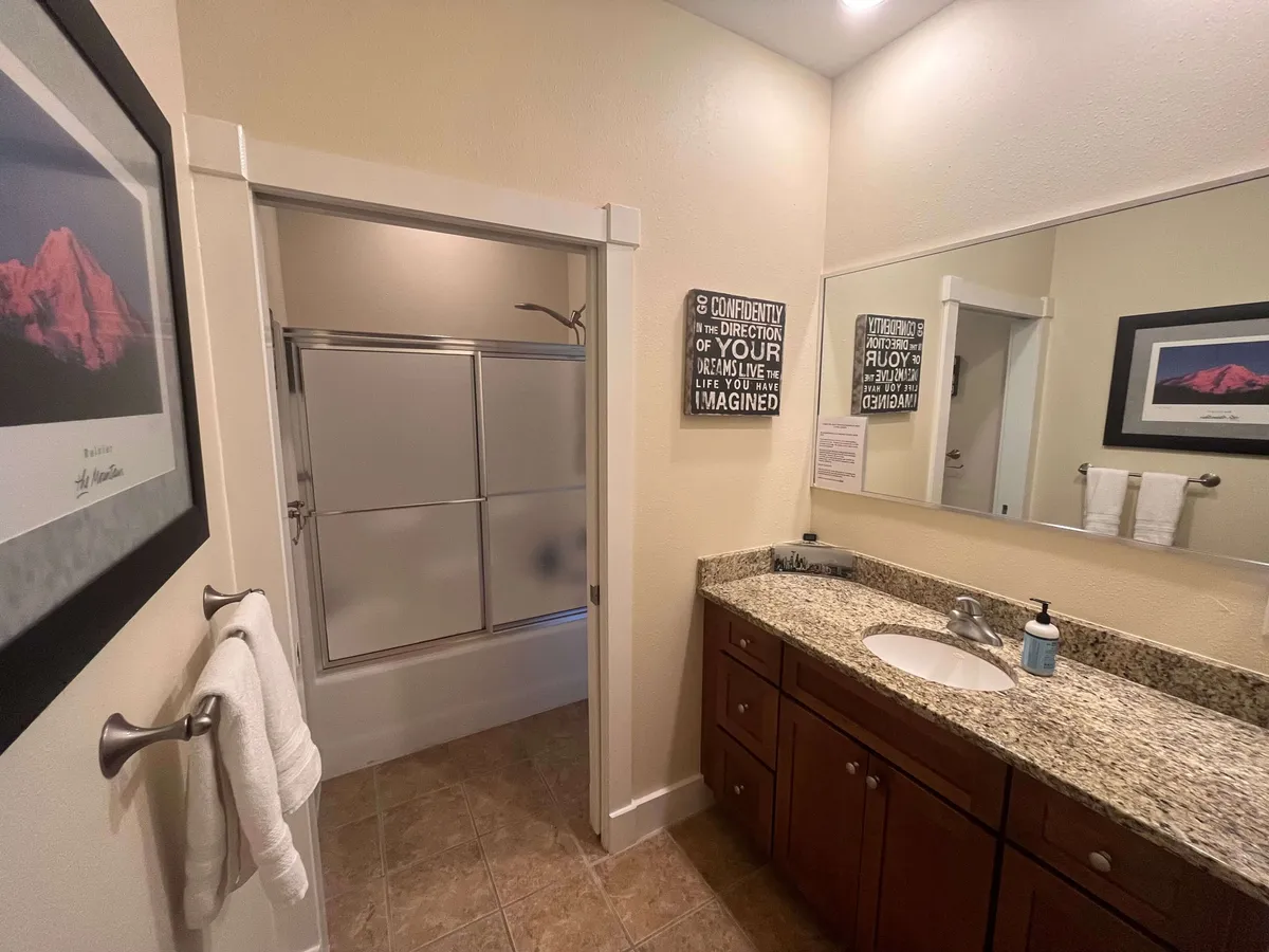 This bathroom scene highlights a granite countertop, a well-lit mirror, a spacious shower area, and tasteful framed artwork. The ambiance feels fresh and inviting, suggesting both practicality and indulgence for morning or evening routines.