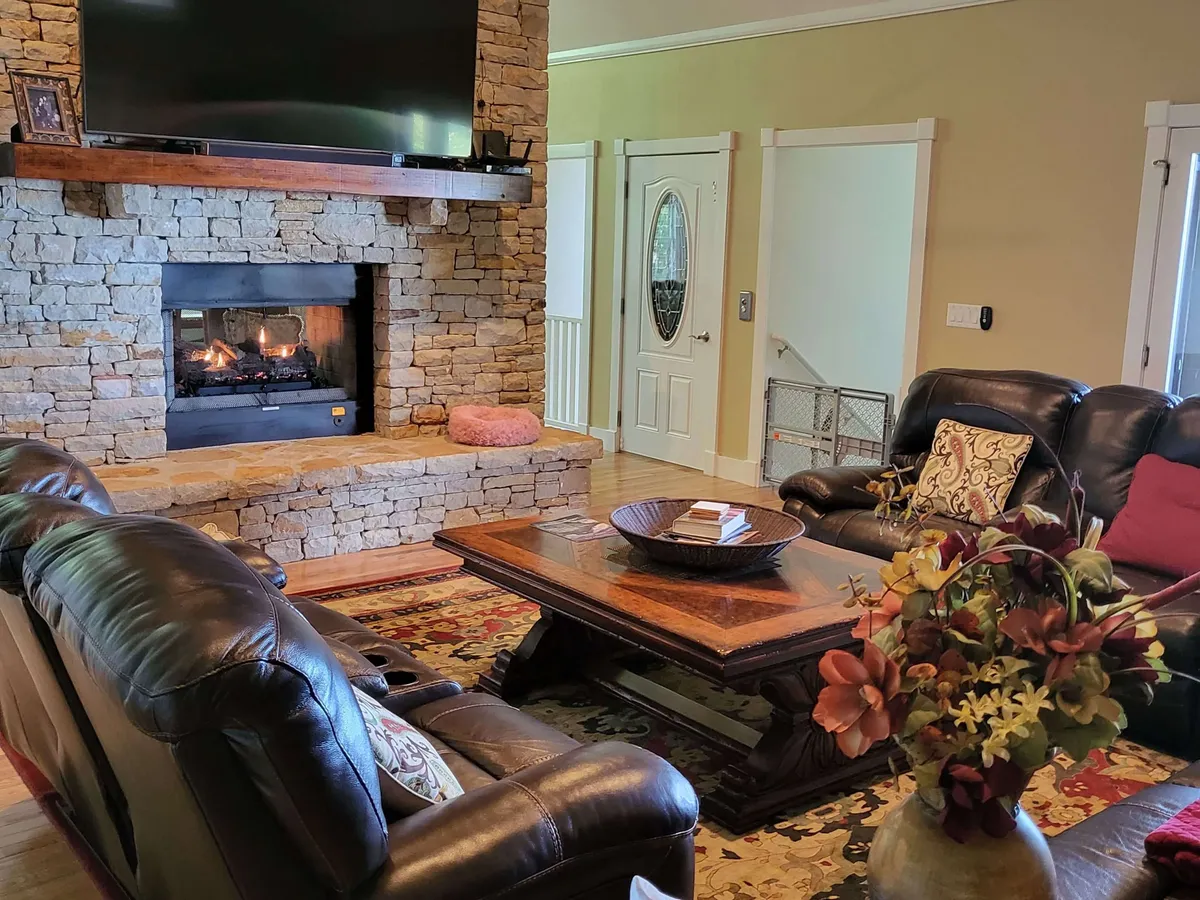 A warm and cozy living room with a central stone fireplace, leather sofas, and decorative pillows. The setting suggests a welcoming space to relax after a day of adventure, ideal for intimate evenings spent by the fire.