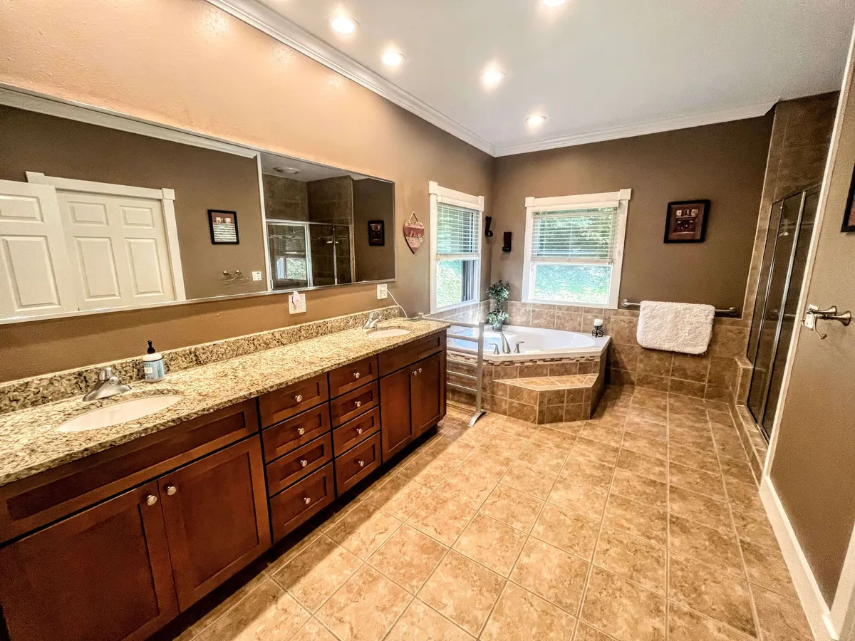A serene, spa-like bathroom featuring a large bathtub, expansive granite countertop with double sinks, a large mirror, and windows that let in abundant natural light. The space feels luxurious and perfect for self-care routines.