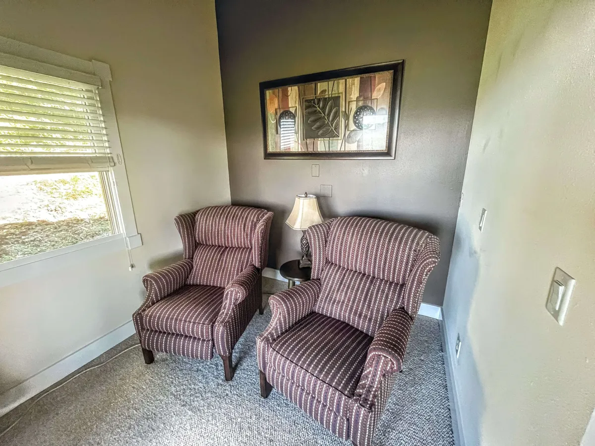 This image features two inviting armchairs flanking a table lamp, with framed artwork adorning the walls. The lighting is warm and the ambiance is cozy, evoking a perfect setting for curling up with a book or enjoying quiet conversation.