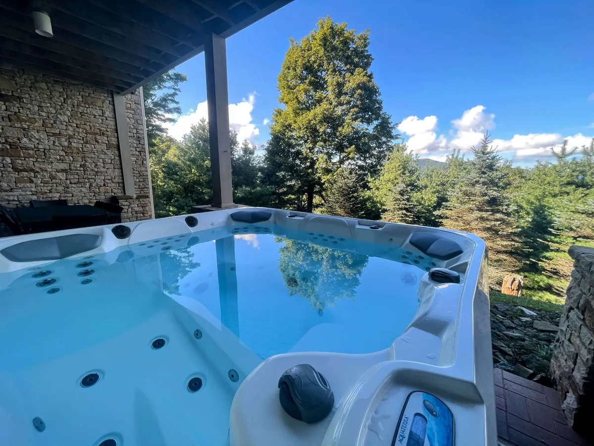 The scene highlights an inviting hot tub set on an exterior deck, surrounded by tall trees and overhead sky. The orientation suggests picturesque sunset or evening stargazing possibilities, making it ideal for intimate or social moments after an adventurous day.
