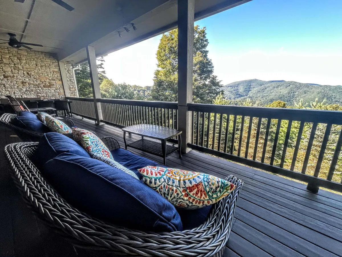 A cozy outdoor seating area with plush pillows is arranged to face out toward breathtaking mountain scenery. The area suggests both morning relaxation and evening gatherings, with soft, ambient lighting enhancing the tranquil atmosphere.
