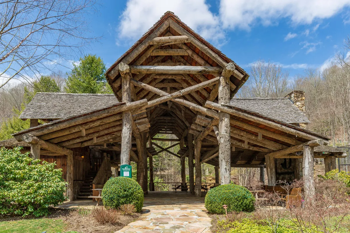 A welcoming exterior shot featuring a wooden structure surrounded by landscaped greenery and a stone pathway, perfect for outdoor gatherings or relaxing. The warm lighting and inviting setup evoke comfort and inclusive socializing across generations.