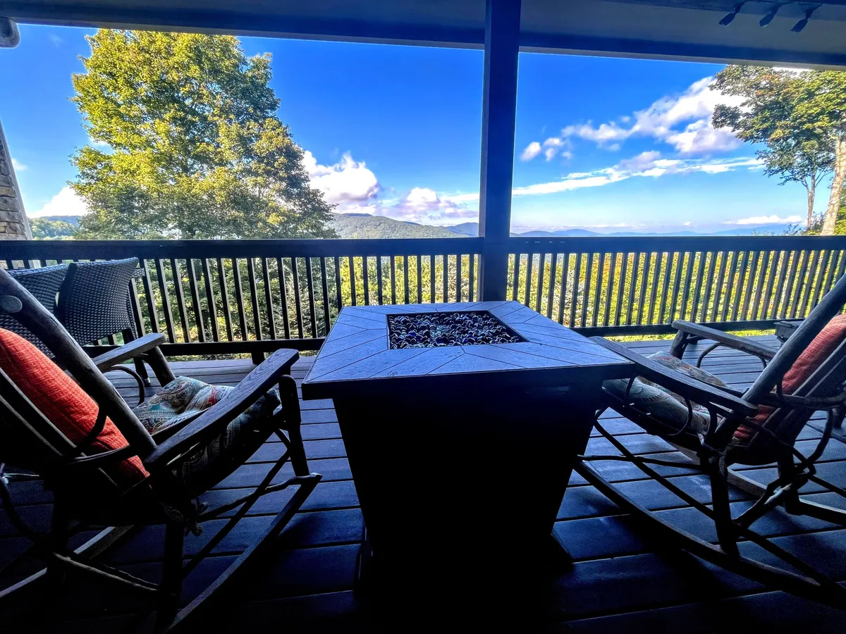 An exterior seating area with rocking chairs surrounding a fire pit table, all overlooking a stunning mountain view. The tranquil mood and setup invite guests to gather and enjoy sunset or stargazing together.