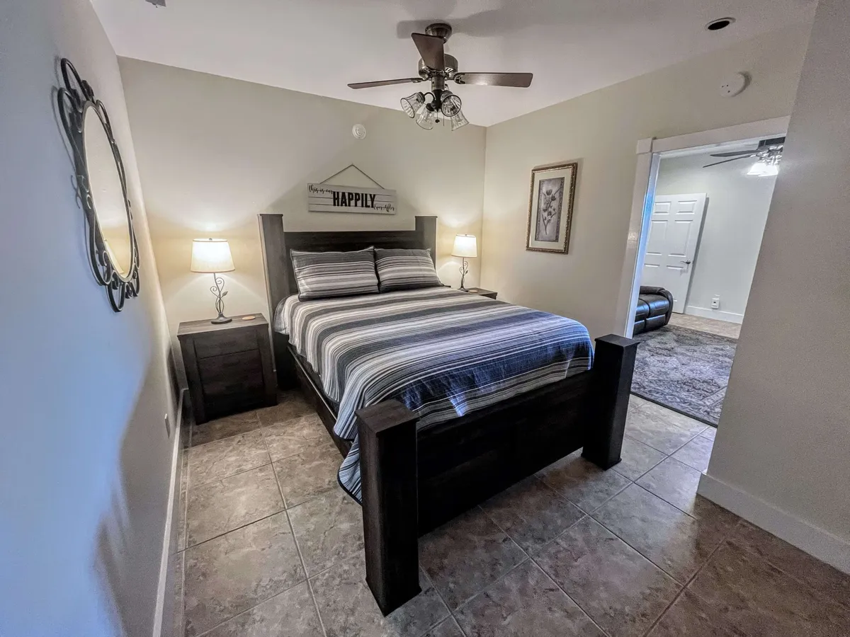 An inviting bedroom with a well-made bed, soft lighting from stylish fixtures, a nightstand, mirror, and tasteful decorative wall art. The ambiance is cozy and ideal for relaxation, reading, or winding down.