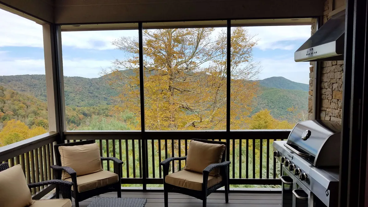 This image features an inviting outdoor seating area complete with a grill, set on a porch overlooking a vast mountain view and vibrant autumn tree. The scene is bathed in soft natural light, suggesting the perfect place for couples to unwind, share a meal, or savor a glass of wine while taking in the stunning sunset over the peaks.
