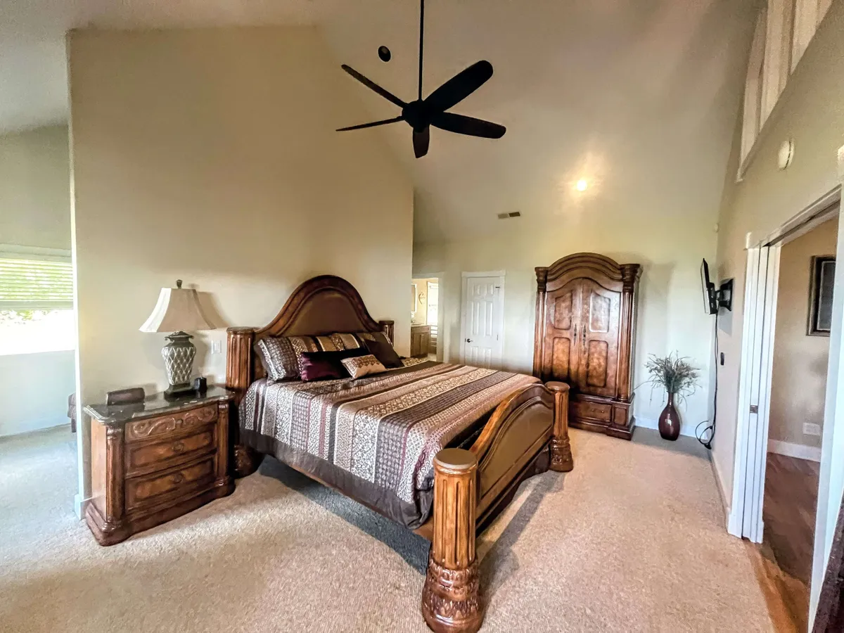 A tranquil bedroom featuring a large wooden bed adorned with plush bedding, a nightstand with an inviting lamp, and a detailed armoire. Soft natural light streams through the window, creating a restful ambiance.