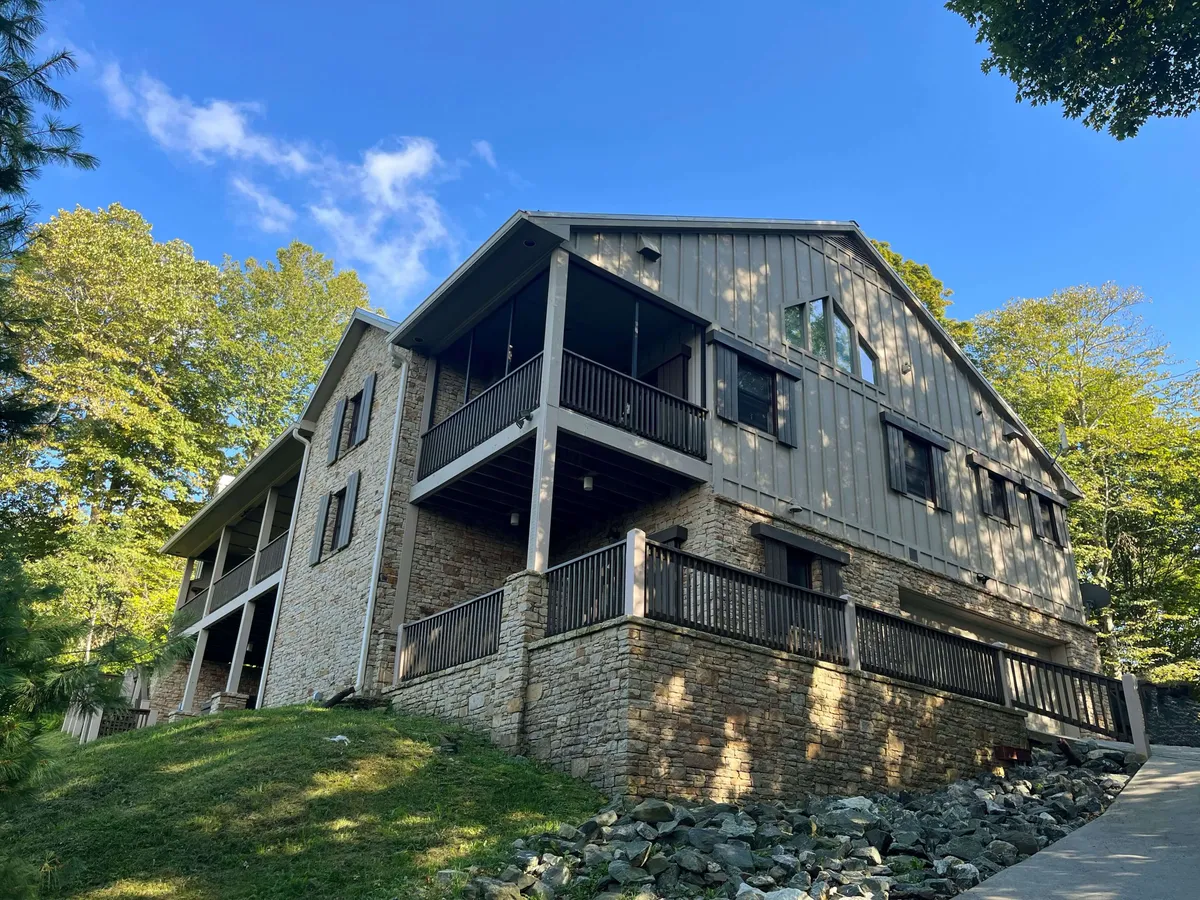 This image showcases the exterior of a luxurious single-family mountain home framed by the lush Blue Ridge Mountains. Multiple balconies invite guests to soak in sweeping sunset views, while expansive porches offer spaces for relaxation and gathering. The serene natural setting envelops the home, hinting at tranquility and a true escape from everyday life.